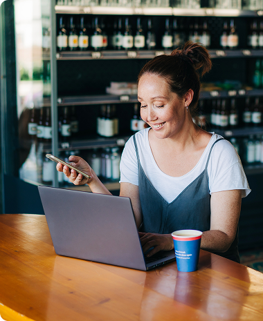 woman using laptop while holding her phone